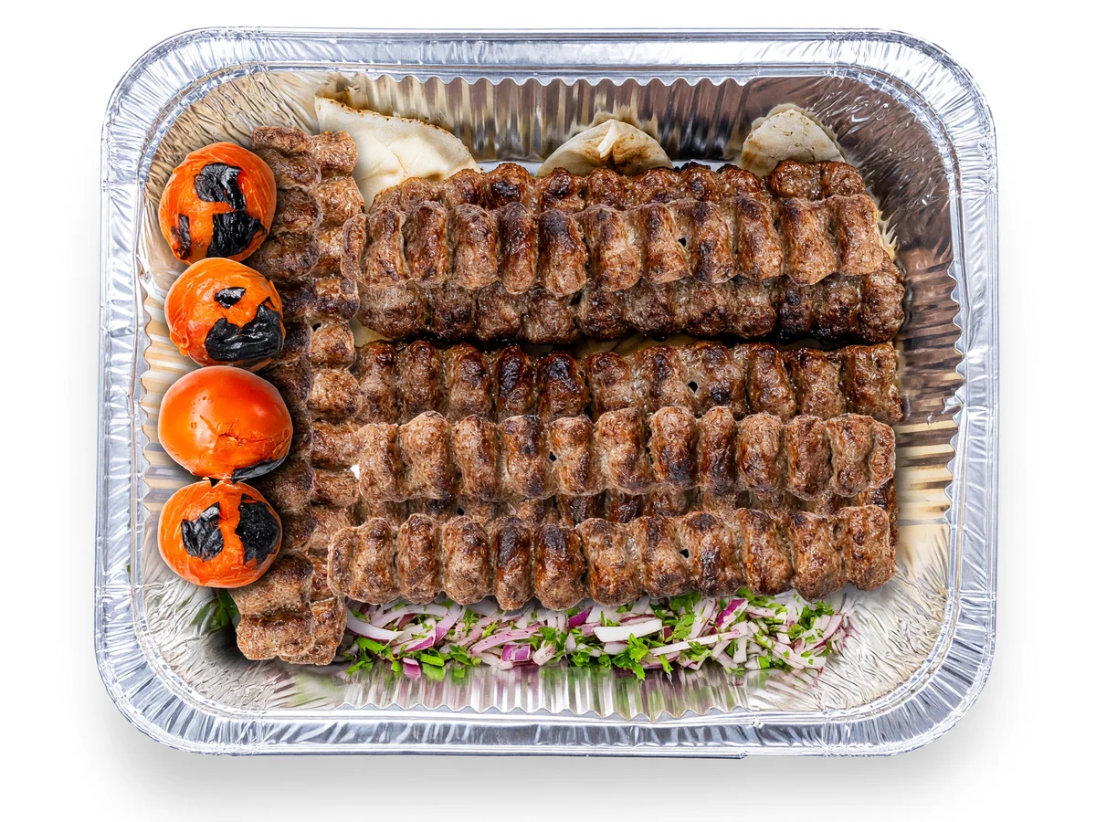 Koobideh family platter: rows of grilled beef koobideh skewers with grilled tomatoes on flatbread in a foil tray at AFRA Grill, Saskatoon