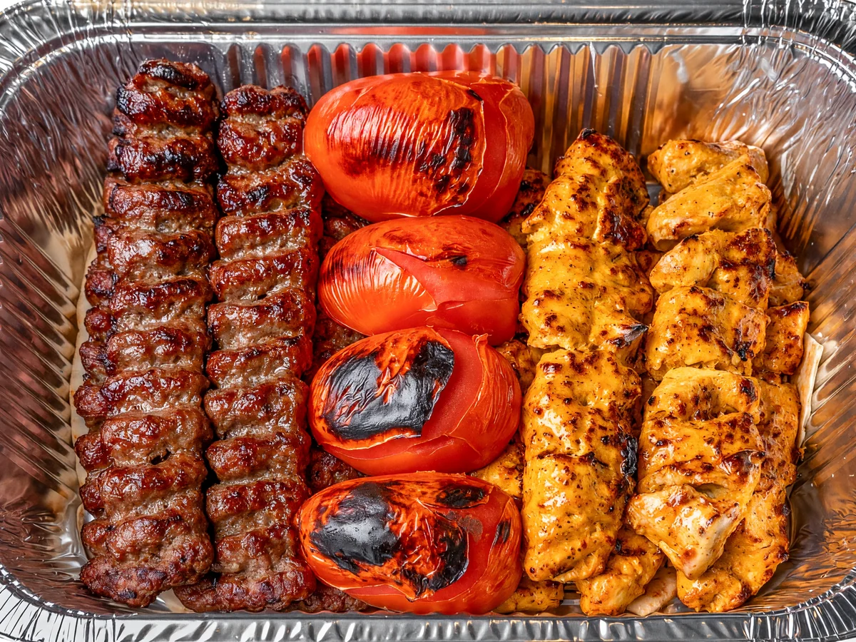 Mixed kabab family platter: beef koobideh skewers, saffron chicken kababs and grilled tomatoes in a large foil tray at AFRA Grill, Saskatoon