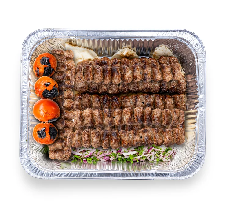 Koobideh family platter: rows of grilled beef koobideh skewers with grilled tomatoes on flatbread in a foil tray at AFRA Grill, Saskatoon