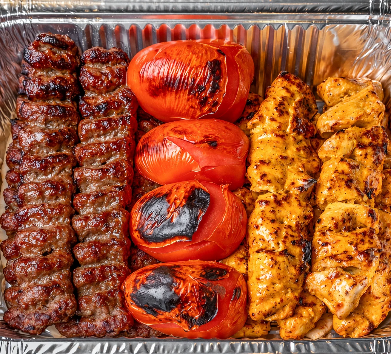 Mixed kabab family platter: beef koobideh skewers, saffron chicken kababs and grilled tomatoes in a large foil tray at AFRA Grill, Saskatoon