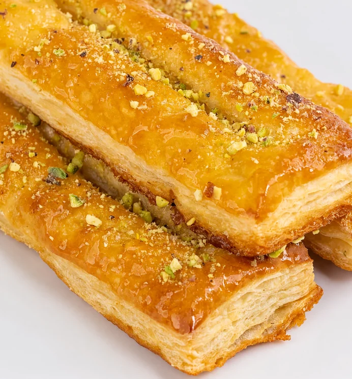 Three glazed zaban puff pastries sprinkled with pistachio on a white plate at AFRA Grill, Saskatoon