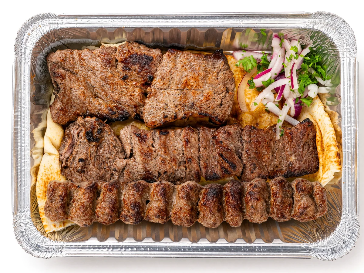 Shazdeh kabab: grilled steak pieces and a beef koobideh skewer on flatbread with sliced onion and herbs in a foil tray at AFRA Grill, Saskatoon